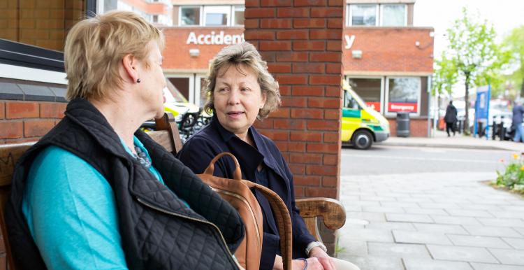 Two women sitting on a bench chatting outside a hospital