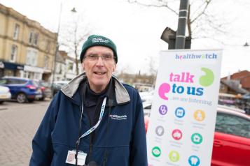 Man wearing a winter hat and stood in front of a Healthwatch banner
