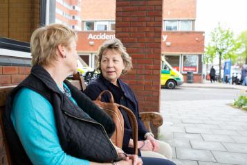 Two women sitting on a bench chatting outside a hospital