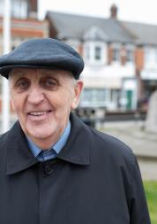 An elderly man wearing a hat smiling at the camera
