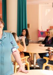 Hospital worker in a room full of patients and family members smiling at the camera