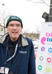 Volunteer standing infront of a banner that says 'talk to us'